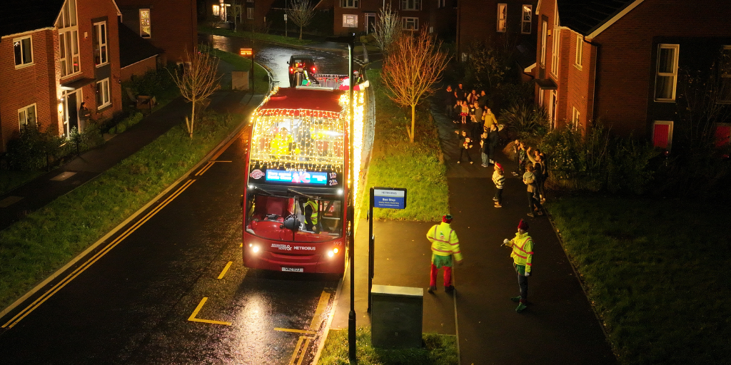 red bus covered in fairy lights pulled up at a stop in a residential area